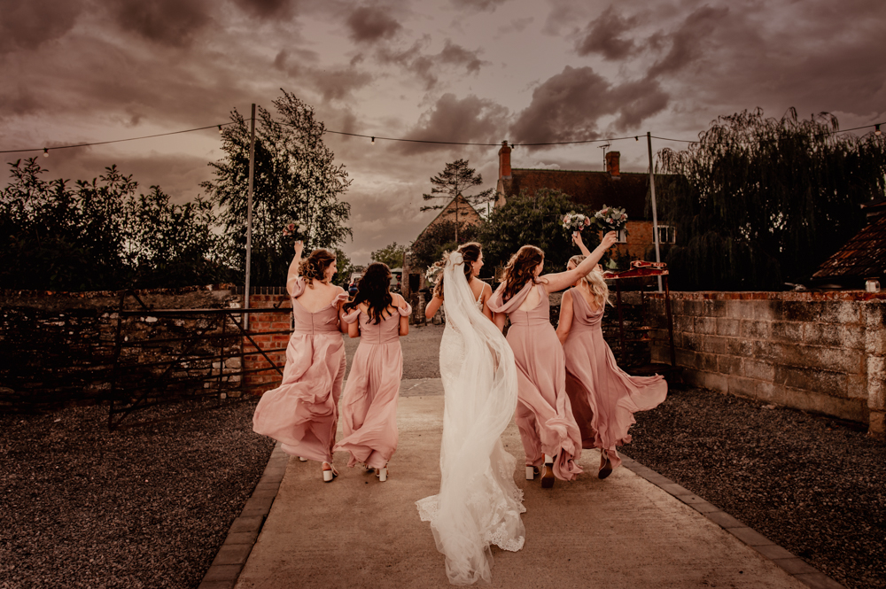 bride and bridesmaids running dramatic sky